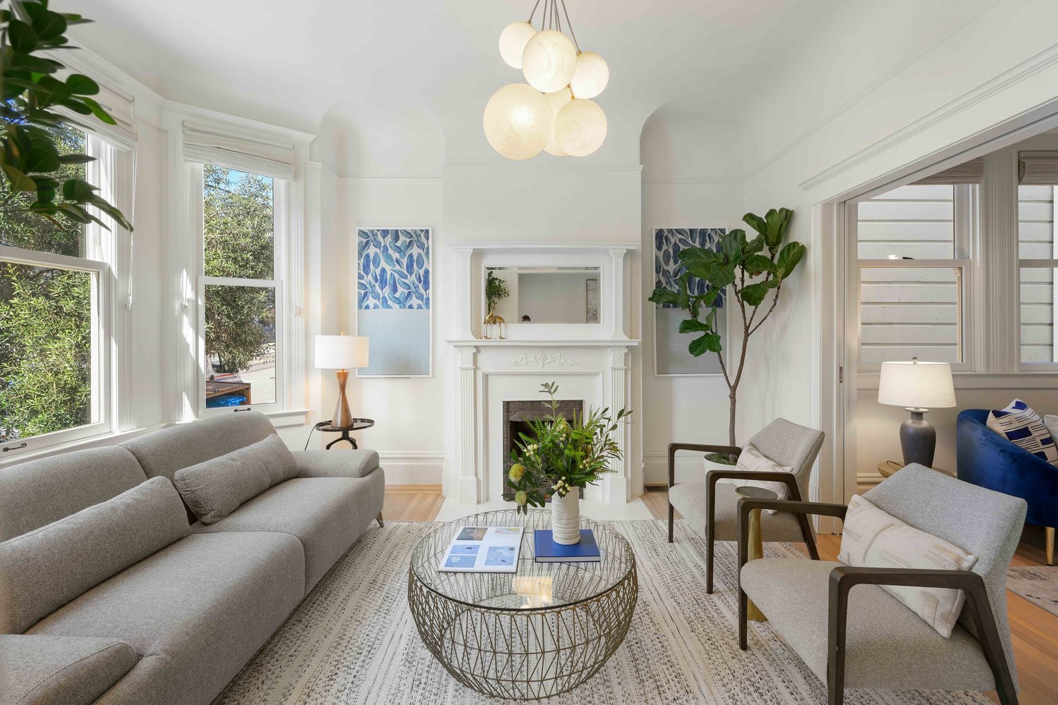 Sun-lit living room styled by Studio Goldfinch with grey sofa, fireplace, and modern chandelier.